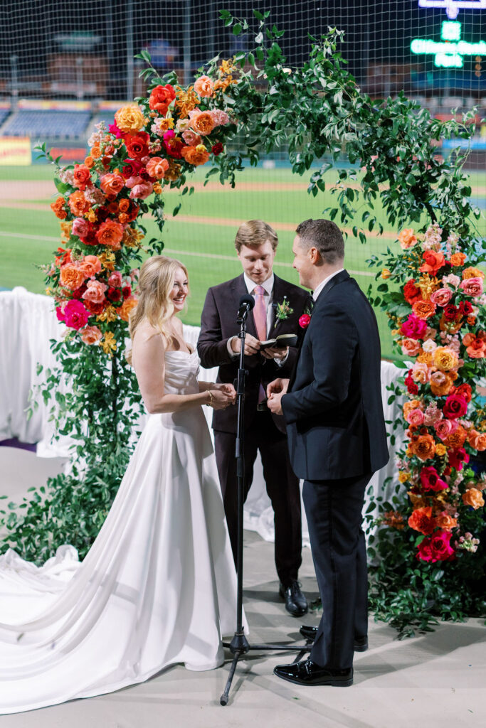 Bride and groom exchange vows during a baseball field wedding ceremony behind home plate at a Citizens Bank Park wedding
