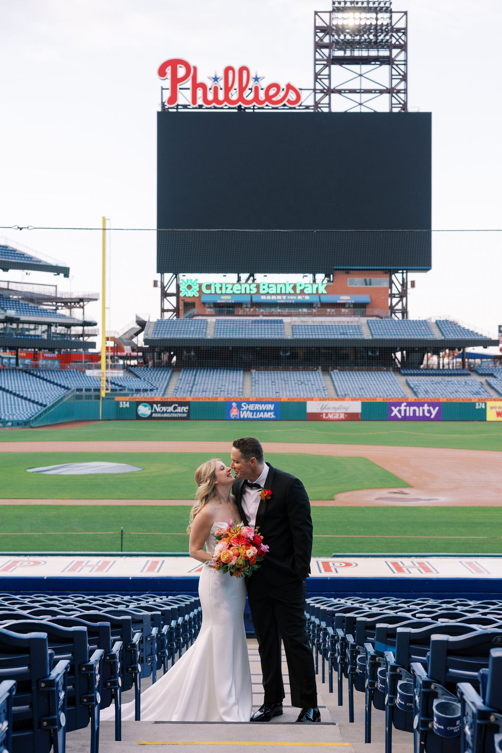 Bride and groom kiss in the stands at Citizens Bank Park in front of the Phillies sign